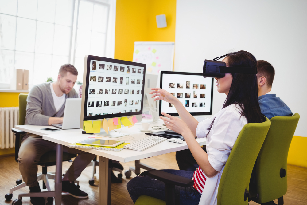 Yoiung female executive enjoying augmented reality headset with colleagues sitting at creative office-1
